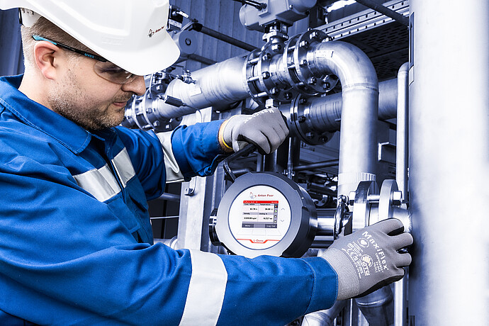 Industrial technician servicing an Anton Paar L-Dens inline density sensor on a stainless steel pipeline in a processing facility.